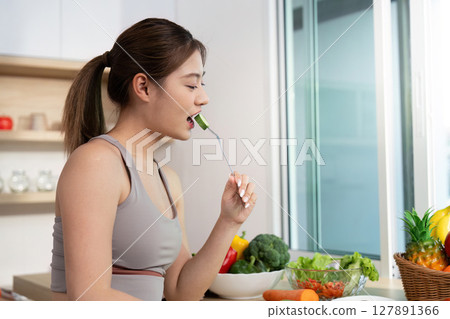 Wellness and Healthy Eating. Young woman enjoying a fresh vegetable snack in a bright kitchen. 127891366