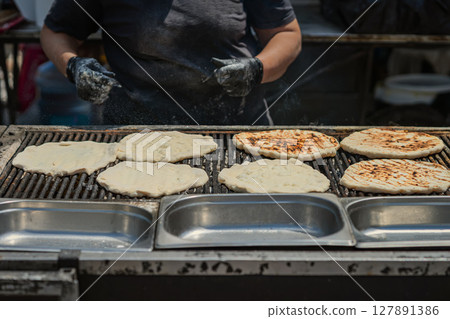 Flatbreads baking on grill at outdoor food stand, partially cooked and charred. Concept of handmade food, street baking, rustic flavor 127891386