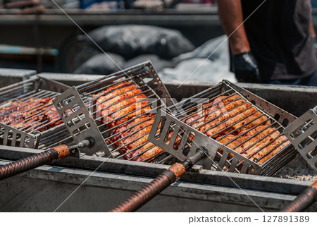 Steaks grilled on iron grill. Grilled meat roasting on open fire in metal baskets at outdoor food stall. Concept of barbecue, street food, smoky flavor Steaks grilled on iron grill. Grilled meat roasting on open fire in metal baskets at outdoor food stall. Concept of barbecue, street food, smoky flavor 127891389