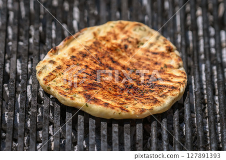 Grilled flatbread cooking over hot coals with golden crust and smoky grill marks. Concept of flatbread preparation and traditional street food flavor 127891393