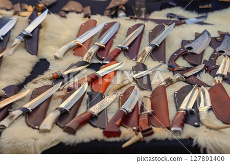 Knives collection Collection of handcrafted knives with leather sheaths displayed on fur-covered table. Concept of craftsmanship, survival tools, rustic design 127891400