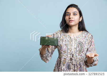 Positive happy girl presenting chroma key isolated screen on device, doing promotion for a commercial against studio background. Upbeat indian person used for advertising brands. 127891523