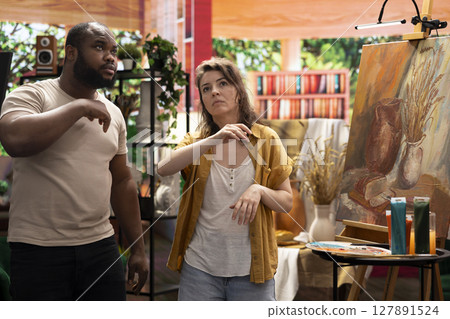 Diverse team of artists sharing their new painting ideas before finishing the artwork, discussing about used painting techniques for a fine art gallery exhibition. Skilled painters in atelier. 127891524