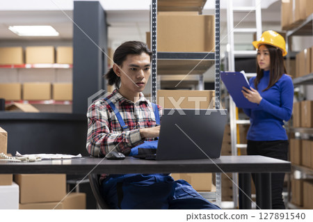 Asian startup employee applies labels and organizes merchandise for delivery. Man sitting at the packaging station to handle all custom orders, small scale fulfillment center. Local brand. 127891540