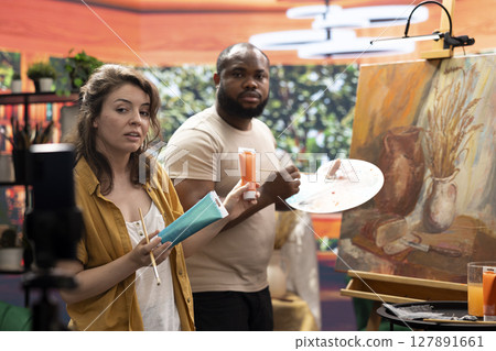 Woman artist hosting an online class to present products and technique used on a rustic artwork, recording a tutorial online. Team of painters doing a master class for e learning, art instruction. 127891661