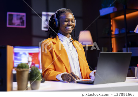 Woman sitting at desk wearing headphones laughing, watching funny TV shows on laptop, streaming content. Person entertained by TV series on chroma key notebook display, selecting episodes 127891663