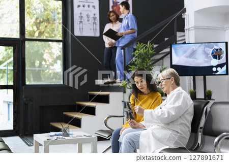 Skilled physician gives advice and explanation of x ray scans to asian patient during a health check in a hospital lobby. Specialist analyzes radiology test results for a recovery plan. Skilled physician gives advice and explanation of x ray scans to asian patient during a health check in a hospital lobby. Specialist analyzes radiology test results for a recovery plan. 127891671