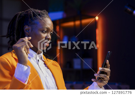Woman relaxing sitting at home office desk, texting friends on smartphone in front of laptop. Freelancer taking break to chat with mates online using phone in living room 127891776