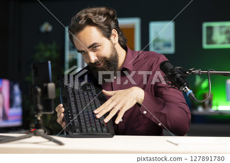 Tech guru promoting mechanical keyboard from sponsor to subscribers. Content creator paid by brand to showcase computer peripheral device with neon lit keys in home studio 127891780