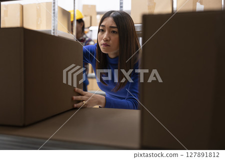 Asian woman preparing custom orders in storage room with parcels and products. Local shipping and retail fulfillment are part of daily business operations in small scale logistics center. Asian woman preparing custom orders in storage room with parcels and products. Local shipping and retail fulfillment are part of daily business operations in small scale logistics center. 127891812