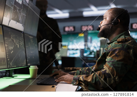 Soldier conducing anti terrorism mission in base of operations employing radar systems to detect and track enemy aircraft. African american specialist studying satellite CCTV visualization Soldier conducing anti terrorism mission in base of operations employing radar systems to detect and track enemy aircraft. African american specialist studying satellite CCTV visualization 127891814