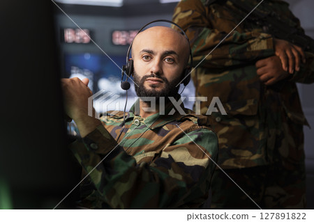 Military agent in war room doing reconnaissance mission, using headset gear. Army expert monitoring counterinsurgency enemy fighters using telecommunication systems to intercept calls 127891822