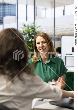 Employer conducting interview with cheerful woman to determine their suitability for company position. Recruiter reviewing happy person resume to determine if necessary qualifications are met 127891838