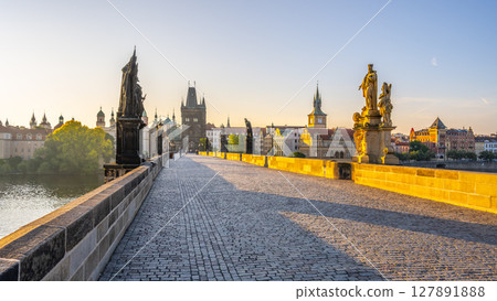 Early morning light casts a warm glow on Charles Bridge in Prague. Statues line the path, while the city awakens with historical buildings reflected in the calm waters of the Vltava River. Early morning light casts a warm glow on Charles Bridge in Prague. Statues line the path, while the city awakens with historical buildings reflected in the calm waters of the Vltava River. 127891888
