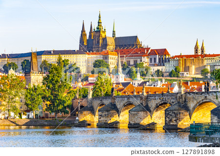 Vibrant colors illuminate Prague Castle above the Vltava River, with the iconic Charles Bridge in the foreground. This serene panorama showcases the beauty of Czechia at dawn. 127891898