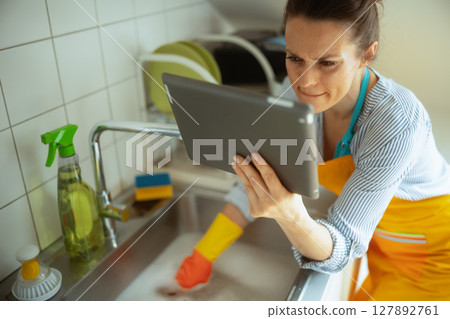 Woman checks tablet to solve kitchen sink blockage 127892761