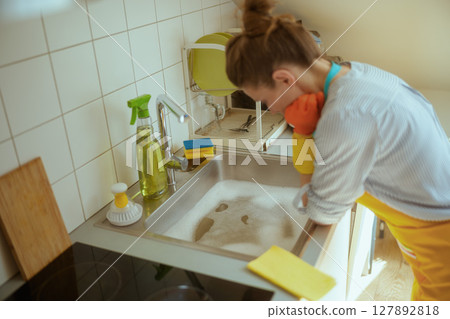 Exhausted woman stares into clogged kitchen sink 127892818