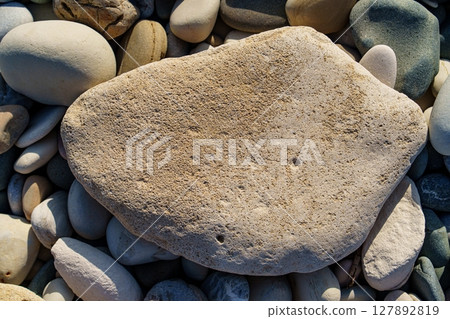 Serene Beachscape Large Stone Amidst Smooth Pebbles on a Sunny Shoreline. Coastal Beauty 127892819