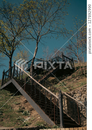 Vintage Outdoor Iron Staircase on a Hill with Trees under Clear Blue Sky 127892990