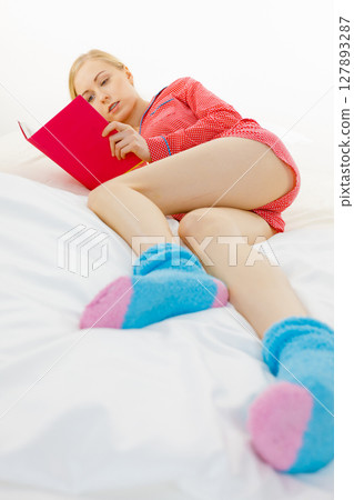 Woman relaxing in bed reading book 127893287