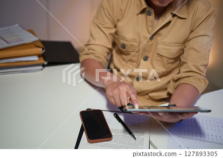 Businessman working overtime, analyzing data on a digital tablet at his office desk Businessman working overtime, analyzing data on a digital tablet at his office desk 127893305