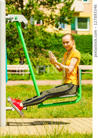 Girl doing exercises outdoor, holding phone 127893346