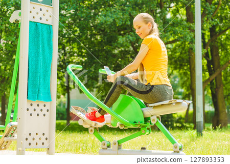 Girl doing exercises outdoor, holding phone 127893353