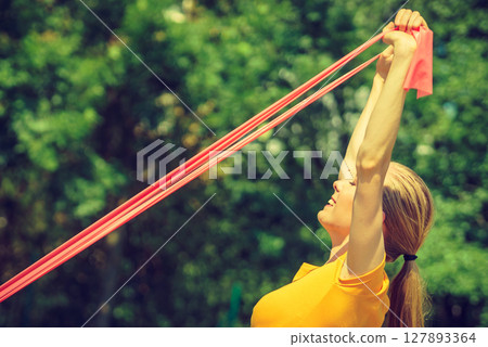 Girl doing exercise outdoor, using resistance fit band. 127893364