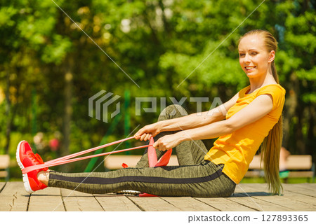 Girl doing exercise outdoor, using resistance fit band. 127893365