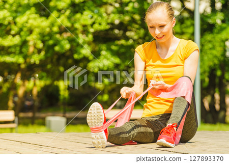 Girl doing exercise outdoor, using resistance fit band. 127893370
