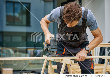 Carpenter working outside with electric jigsaw and small dog in backyard 127893410