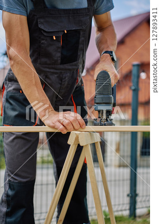 Carpenter working outside with electric jigsaw and small dog in backyard 127893411