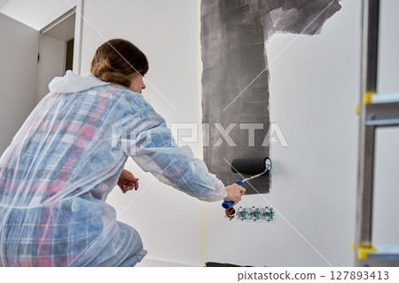 Woman painting white wall with black paint using roller during home renovation Woman painting white wall with black paint using roller during home renovation 127893413