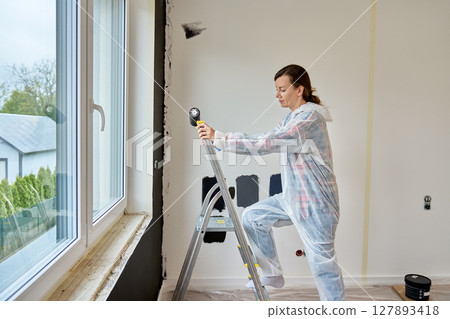 Woman preparing to paint interior wall during apartment renovation Woman preparing to paint interior wall during apartment renovation 127893418