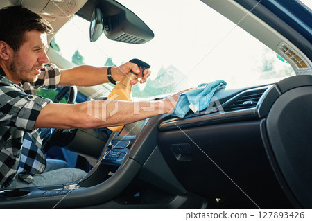 Man Cleaning Car Dashboard with Spray and Cloth 127893426