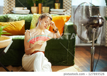Woman Uses Hand Fan and Electric Fan for Heat 127893526