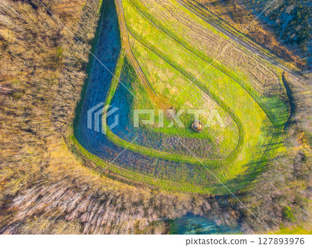 An aerial perspective shows a meticulously shaped artificial hill surrounded by lush greenery. The gentle curves and patterns create a striking visual contrast against the natural surroundings. 127893976