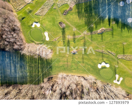 Stunning aerial perspective showcasing a well-maintained golf course with manicured greens, sand traps, and water hazards, nestled among trees during daytime. 127893979