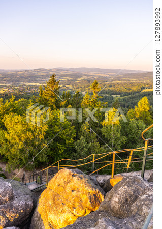 Visitors enjoy the breathtaking sunset from the lookout at Popov Cliffs in the Lusatian Mountains, surrounded by lush greenery and sandstone rock formations. 127893992