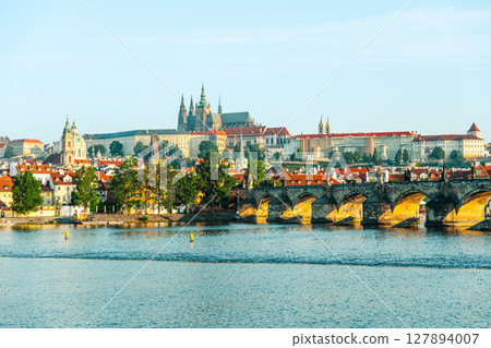 Discover the stunning architecture of Prague Castle overlooking the Vltava River and the iconic Charles Bridge. This clear day showcases the city's historical charm and landscape beauty. 127894007