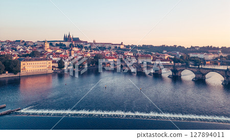 Golden light bathes the medieval architecture of Prague at sunrise, showcasing the Vltava River and the iconic Charles Bridge. Hradcany Castle stands majestically on the hill in the background. Golden light bathes the medieval architecture of Prague at sunrise, showcasing the Vltava River and the iconic Charles Bridge. Hradcany Castle stands majestically on the hill in the background. 127894011