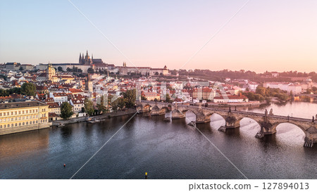 The morning light casts a warm glow over Prague, illuminating the Vltava River and the historic architecture, including Charles Bridge and Hradcany Castle, in a breathtaking panorama. 127894013