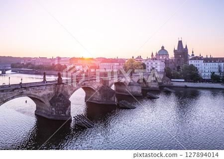 Early morning light bathes Charles Bridge in a golden hue. The iconic Old Town Bridge Tower rises above the Vltava River, creating a picturesque view of Prague's historic architecture. 127894014