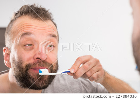Man brushing his teeth in bathroom 127894036