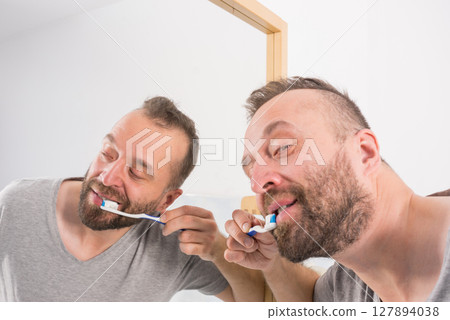 Man brushing his teeth in bathroom Man brushing his teeth in bathroom 127894038