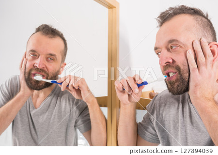 Bored guy brushing his teeth in bathroom Bored guy brushing his teeth in bathroom 127894039