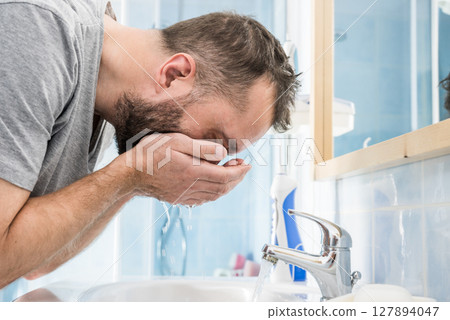 Man washing his face in bathroom 127894047