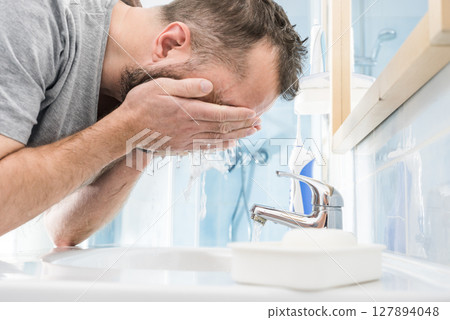 Man washing his face in bathroom 127894048