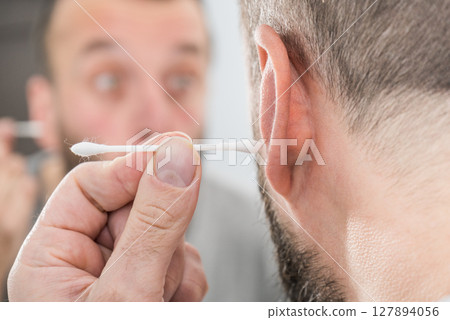 Man removing wax from ear using Q-tip 127894056