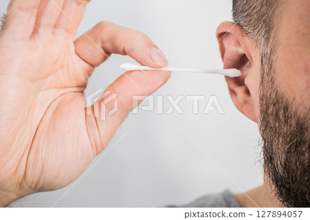 Man removing wax from ear using Q-tip 127894057